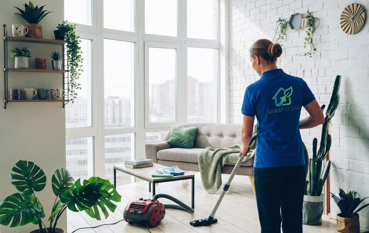 A uniformed Quest Clean specialist vacuuming a bright, plant-filled living room
